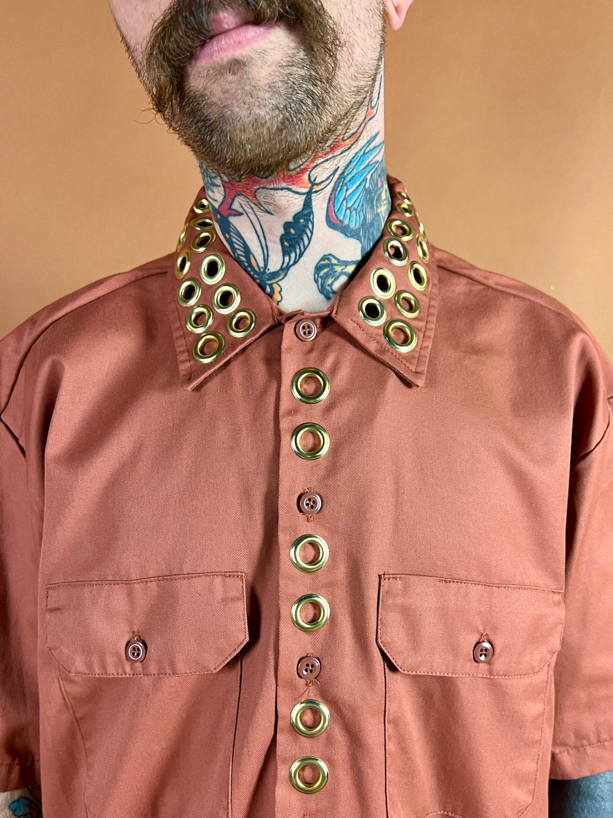 A person with a tattooed neck wearing a shirt with large grommets on the collar and button line.