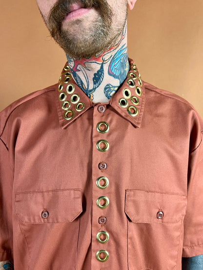 A person with a tattooed neck wearing a shirt with large grommets on the collar and button line.