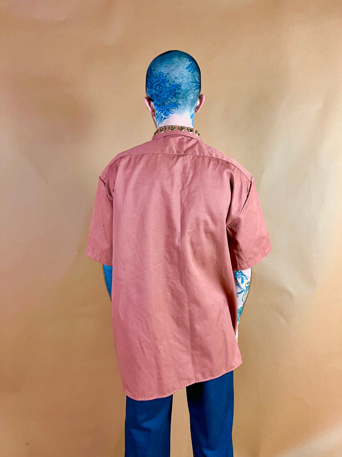 Person with blue hair and tattoos standing with their back to the camera.