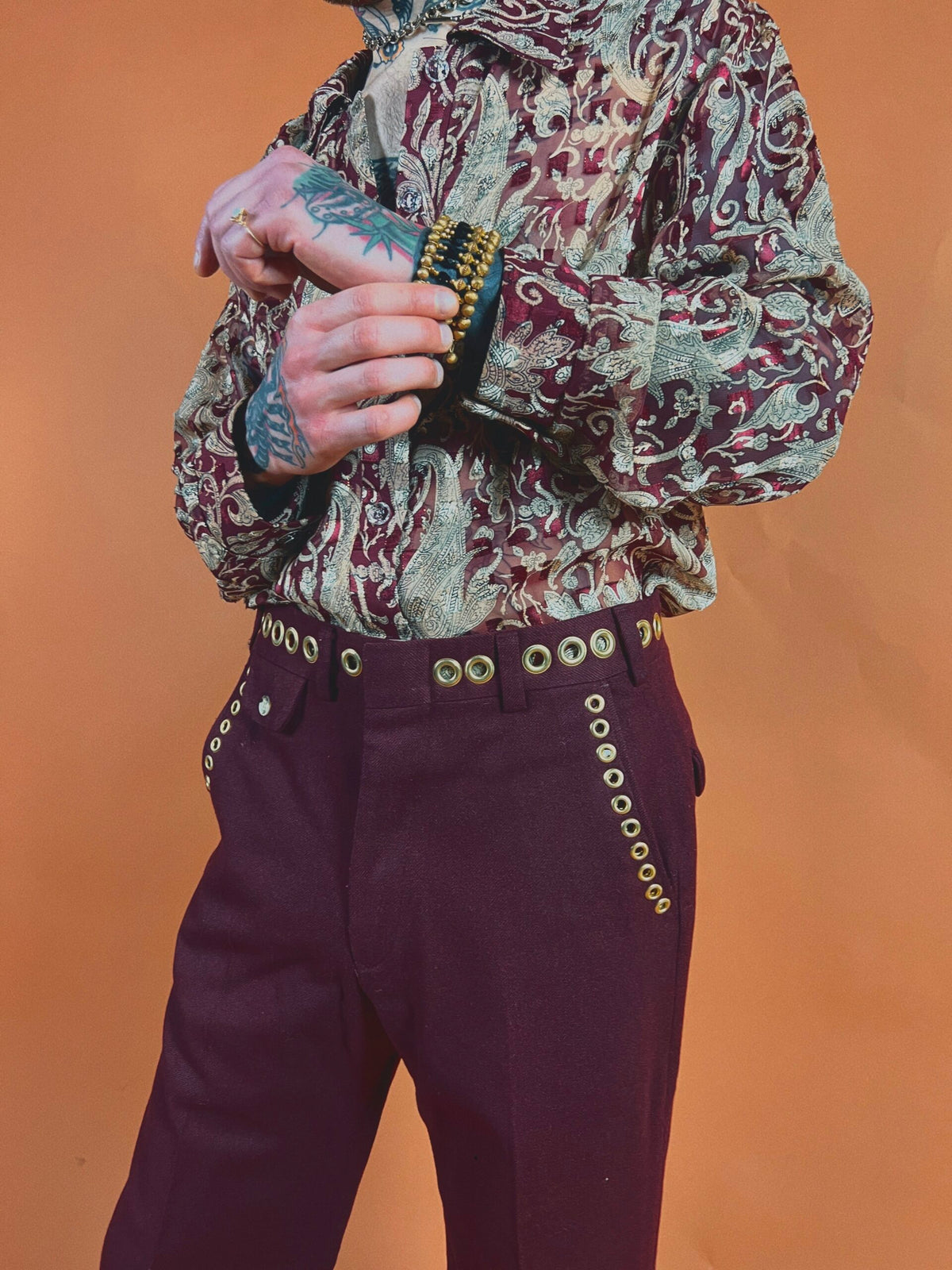 Person in a paisley shirt and burgundy pants with a tattooed hand holding a comb.