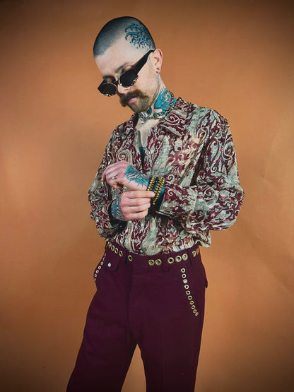 A stylish man in a paisley shirt and maroon trousers checking the time on his watch.