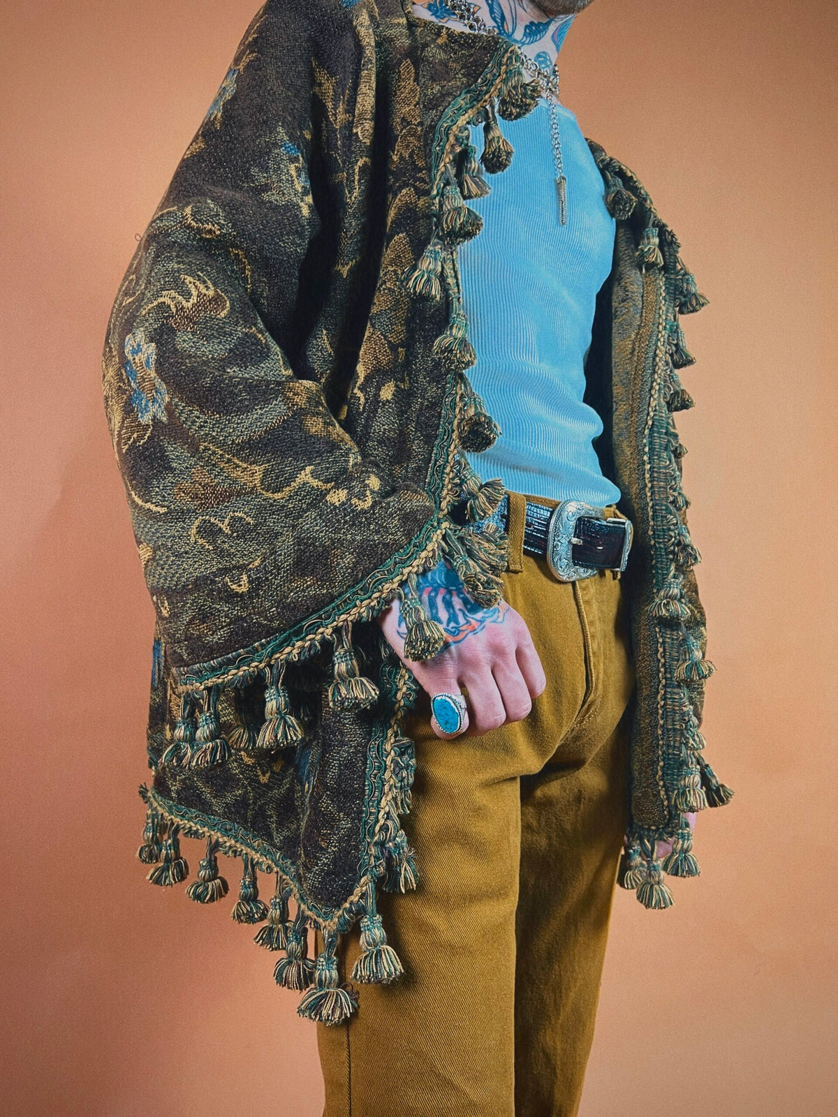 Person in eclectic attire with patterned shawl, mustard pants, and accessorized with jewelry.