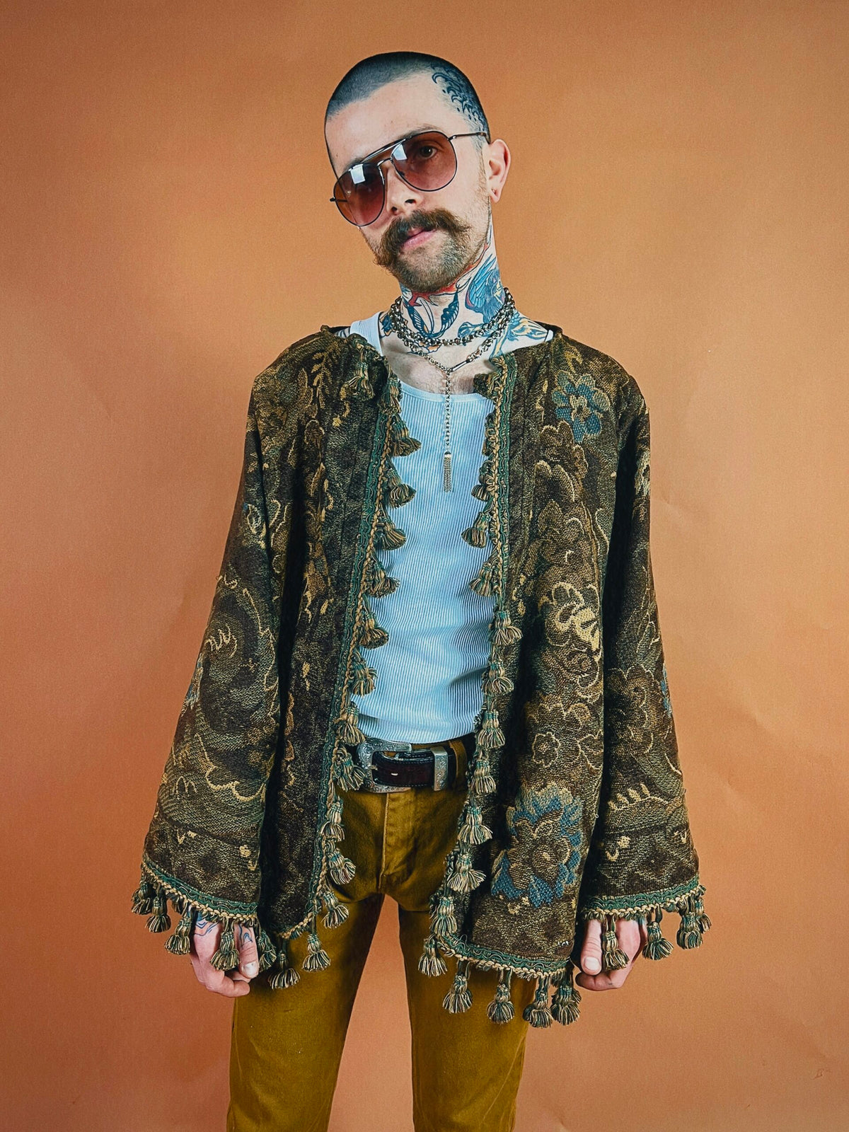 Man in vintage-style clothing with sunglasses posing against an orange background.