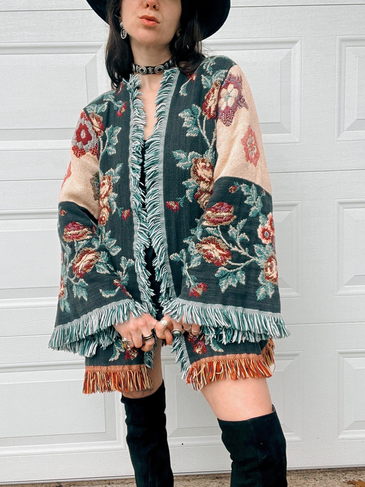 A person in a floral patterned poncho and black hat standing in front of a white door.