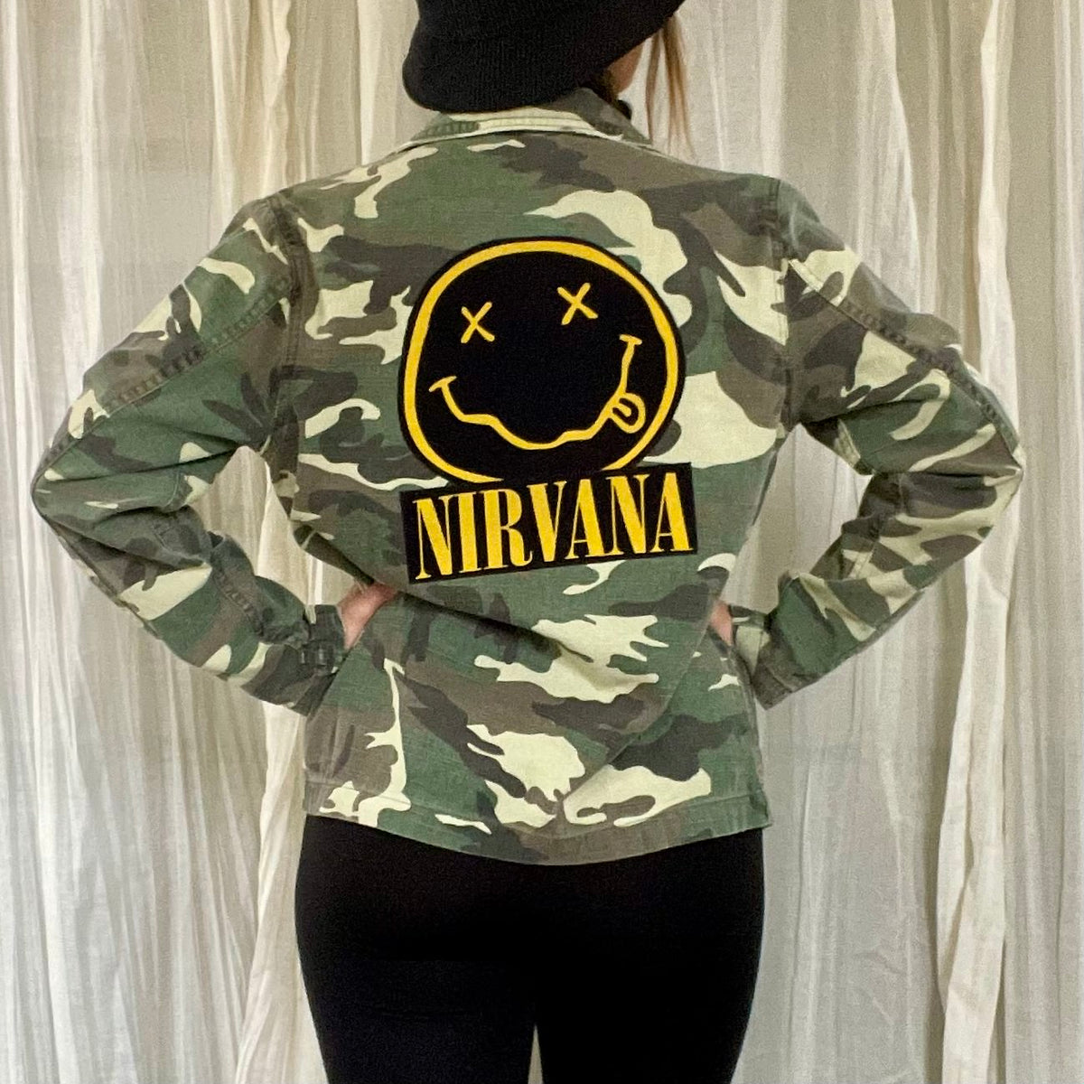A woman wearing a camo jacket with a smiley face on it.