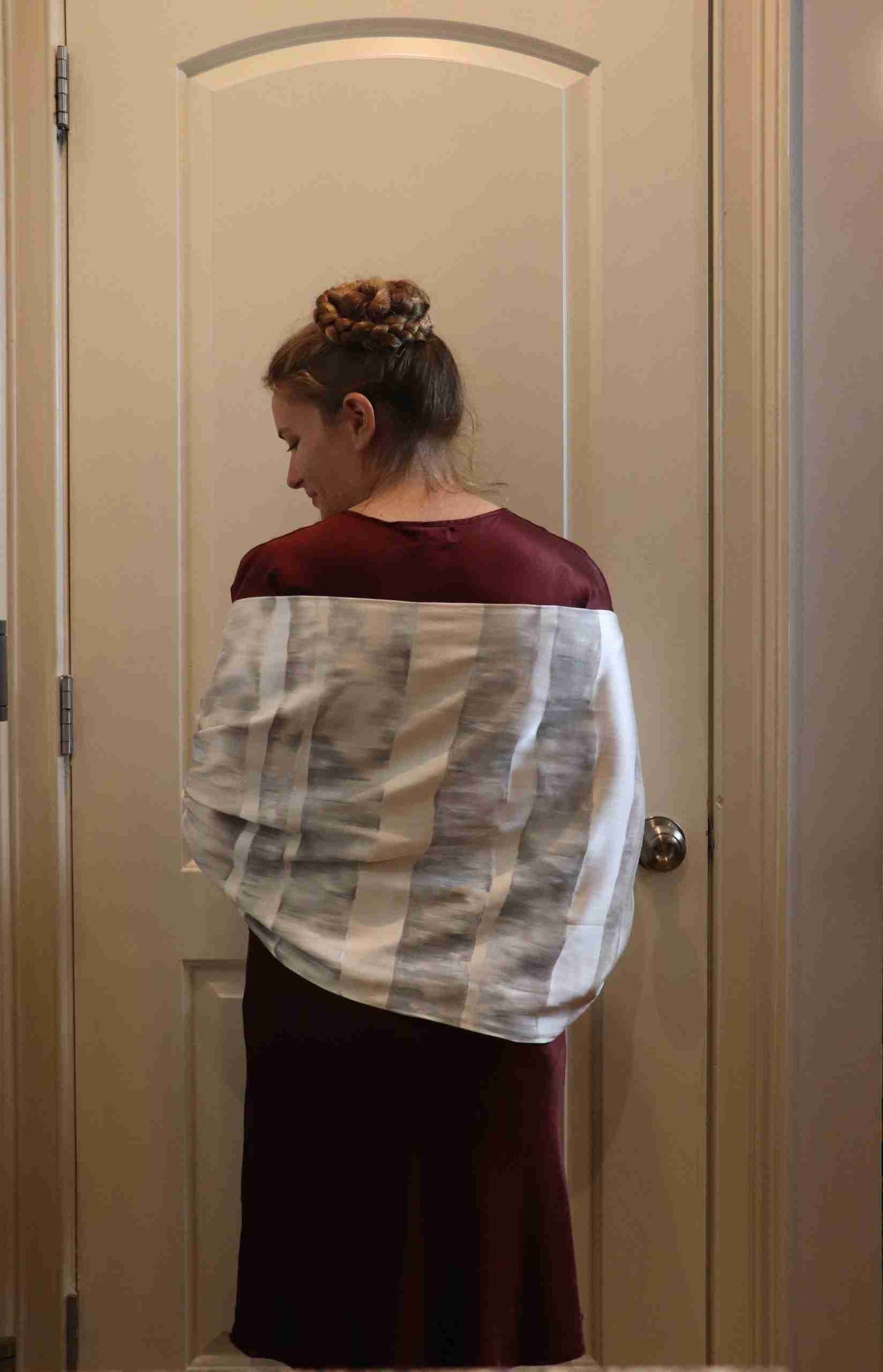 a woman standing in front of a door with a white and black scarf on her.