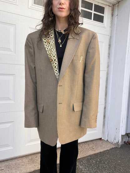 A person wearing an oversized houndstooth blazer and black trousers stands in front of a white garage door.
