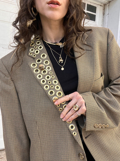 Woman wearing a houndstooth blazer with gold button details and layered necklaces.