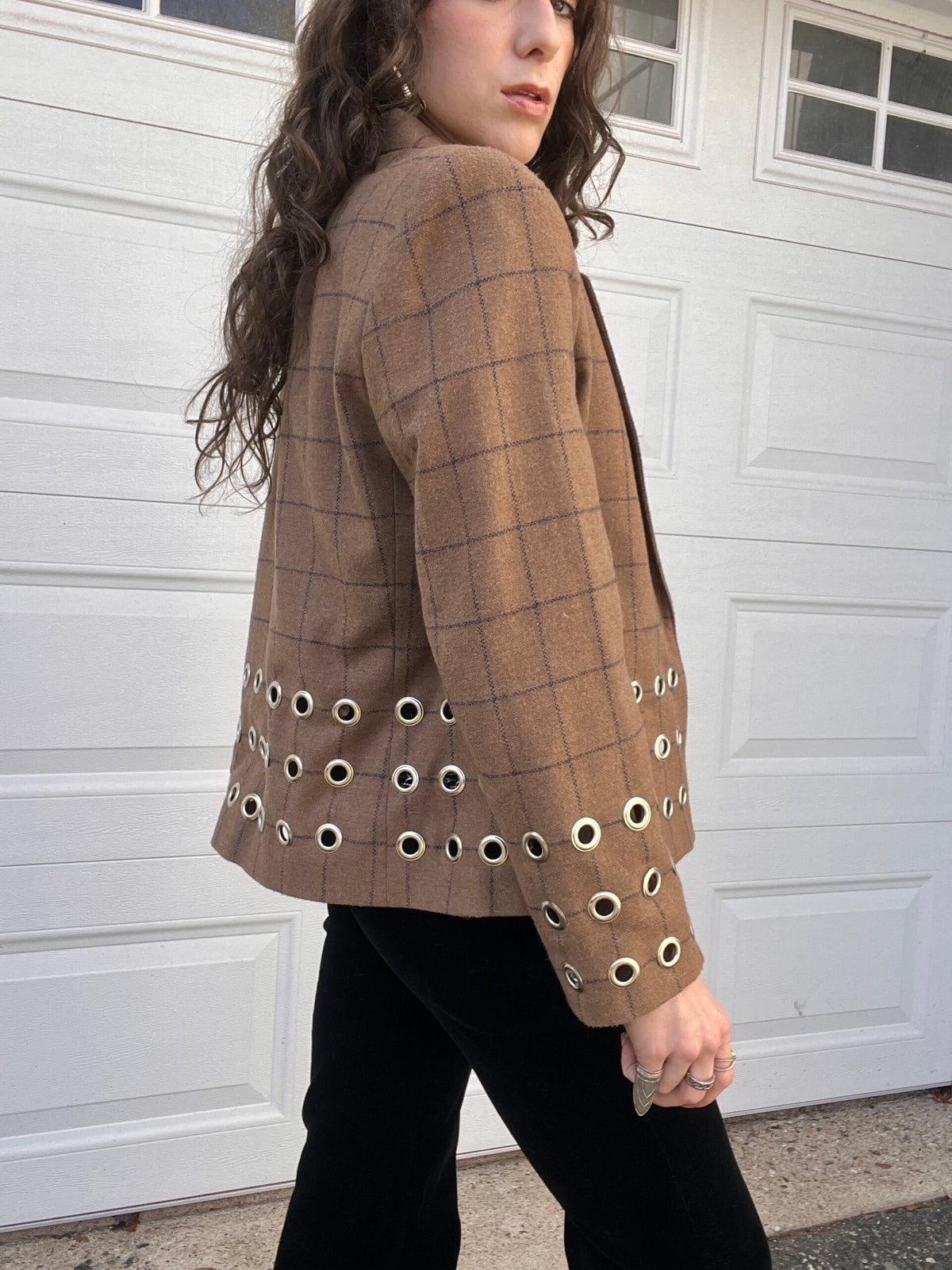 A woman in a plaid blazer with eyelet details on the sleeves standing in front of a white garage door.