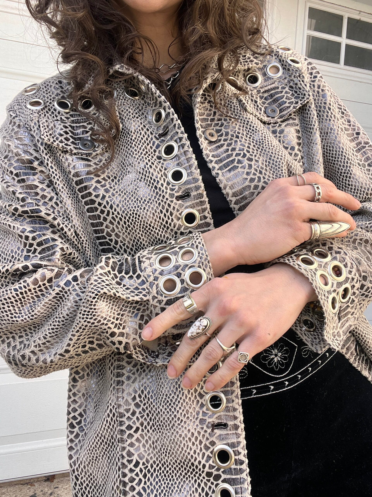 A person wearing a textured jacket with eyelet details, adorned with multiple rings on their fingers.