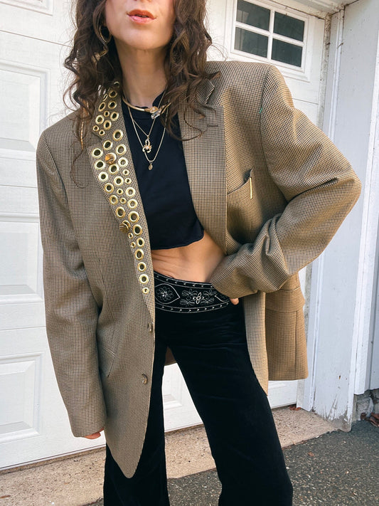 A person in a black crop top and high-waisted pants, wearing a patterned oversized blazer and layered necklaces.