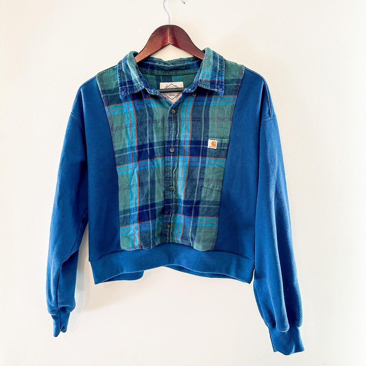 A blue and green plaid sweater hanging on a wall.
