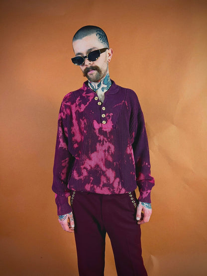 Man in a patterned purple shirt and sunglasses posing against an orange background.