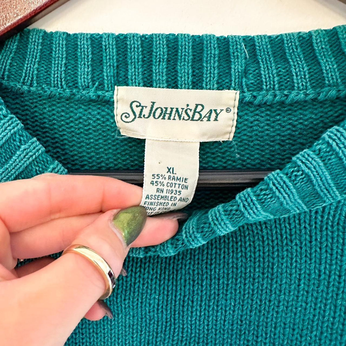 A person wearing a teal sweater with a label on it.