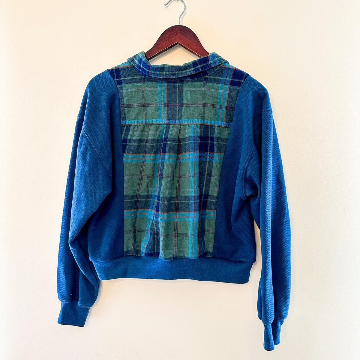 A blue and green plaid sweatshirt hanging on a wall.