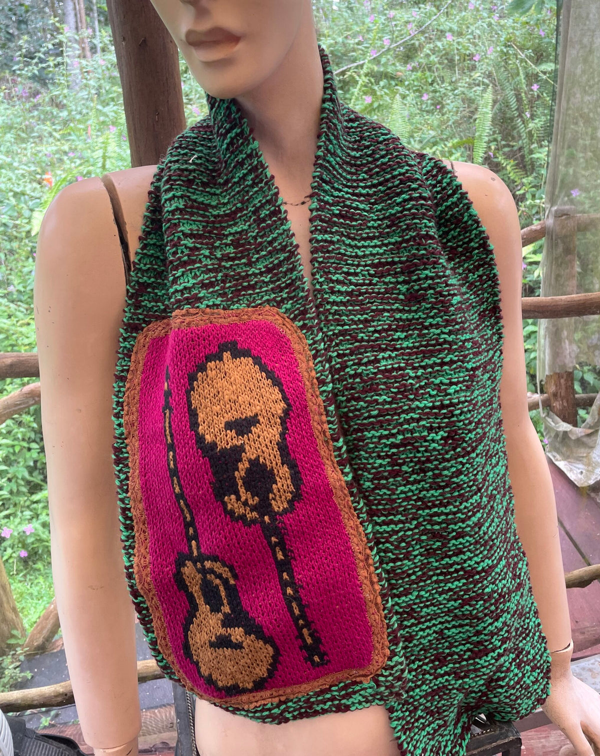 A mannequin wearing a knitted scarf with a guitar on it.