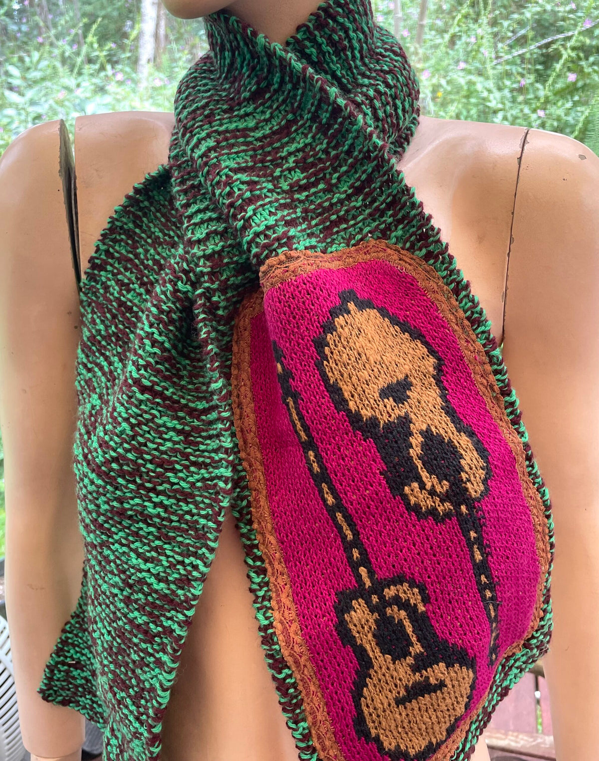 A mannequin wearing a knitted scarf with a guitar on it.
