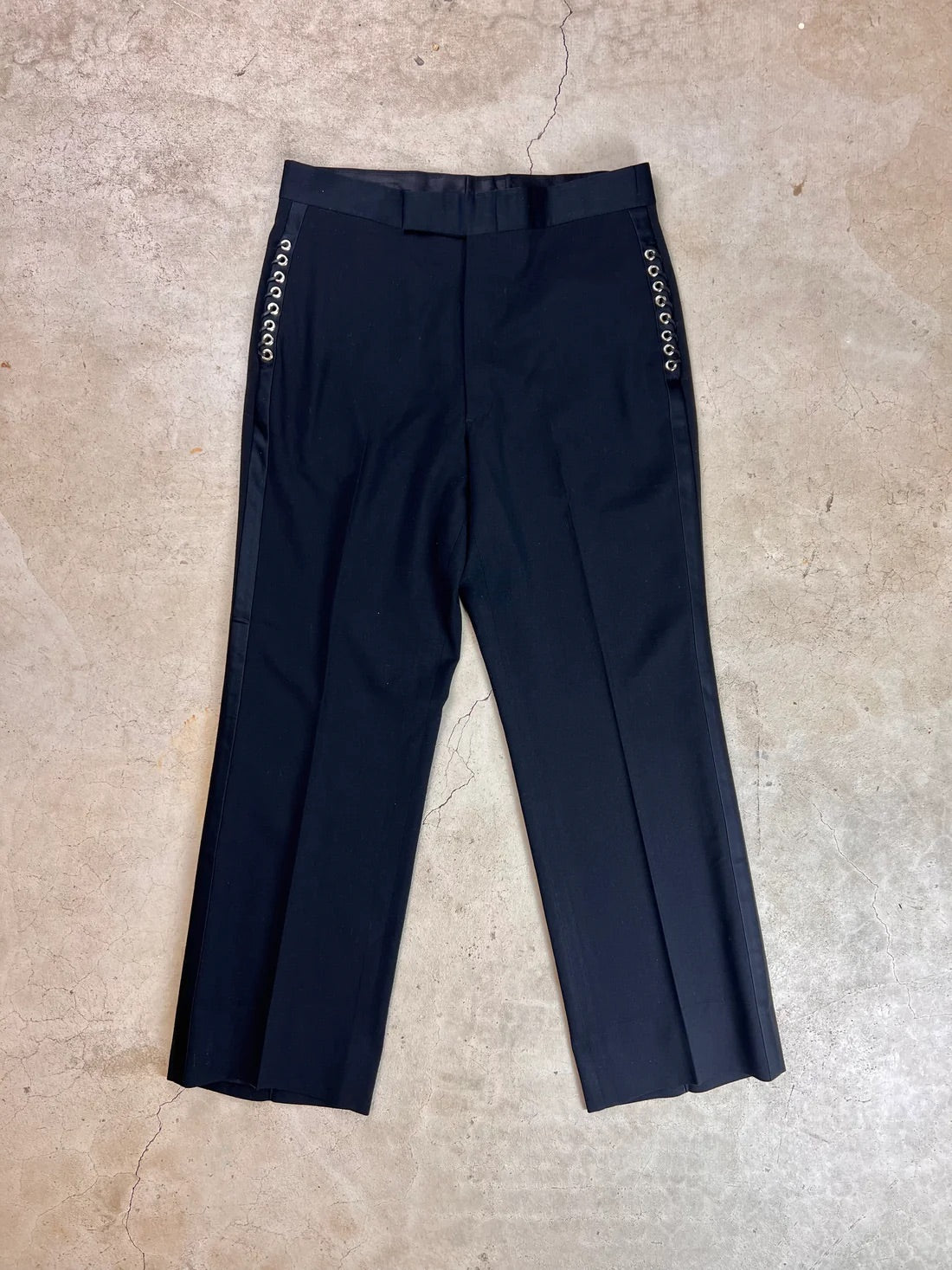 A pair of black trousers with patterned side stripes lying flat on a textured surface.