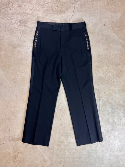 A pair of black trousers with patterned side stripes lying flat on a textured surface.
