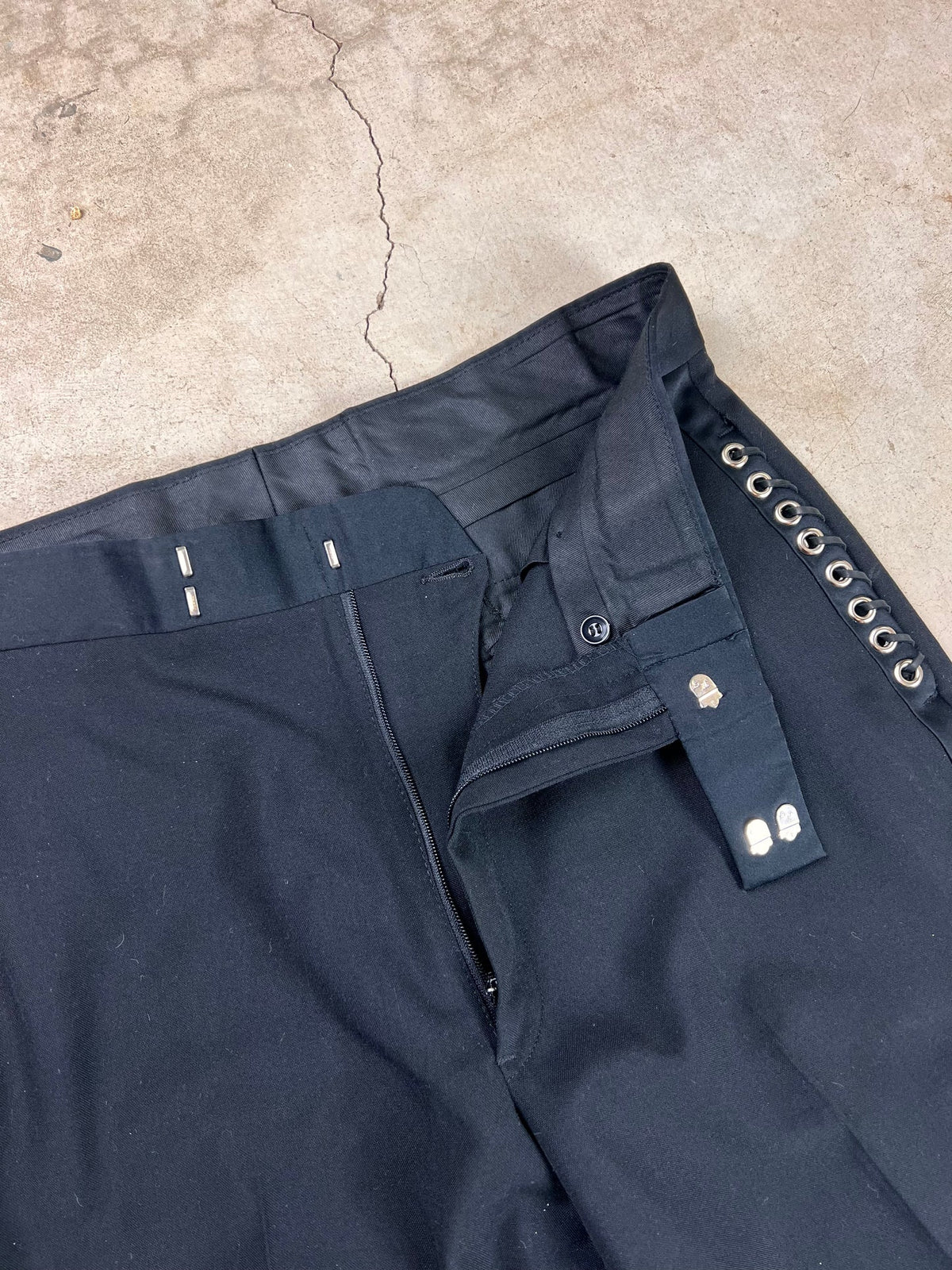 Black trousers with silver eyelet detail on concrete surface.