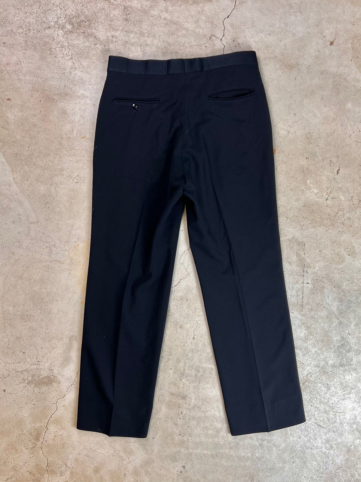 A pair of navy blue dress pants laid flat on a concrete surface.