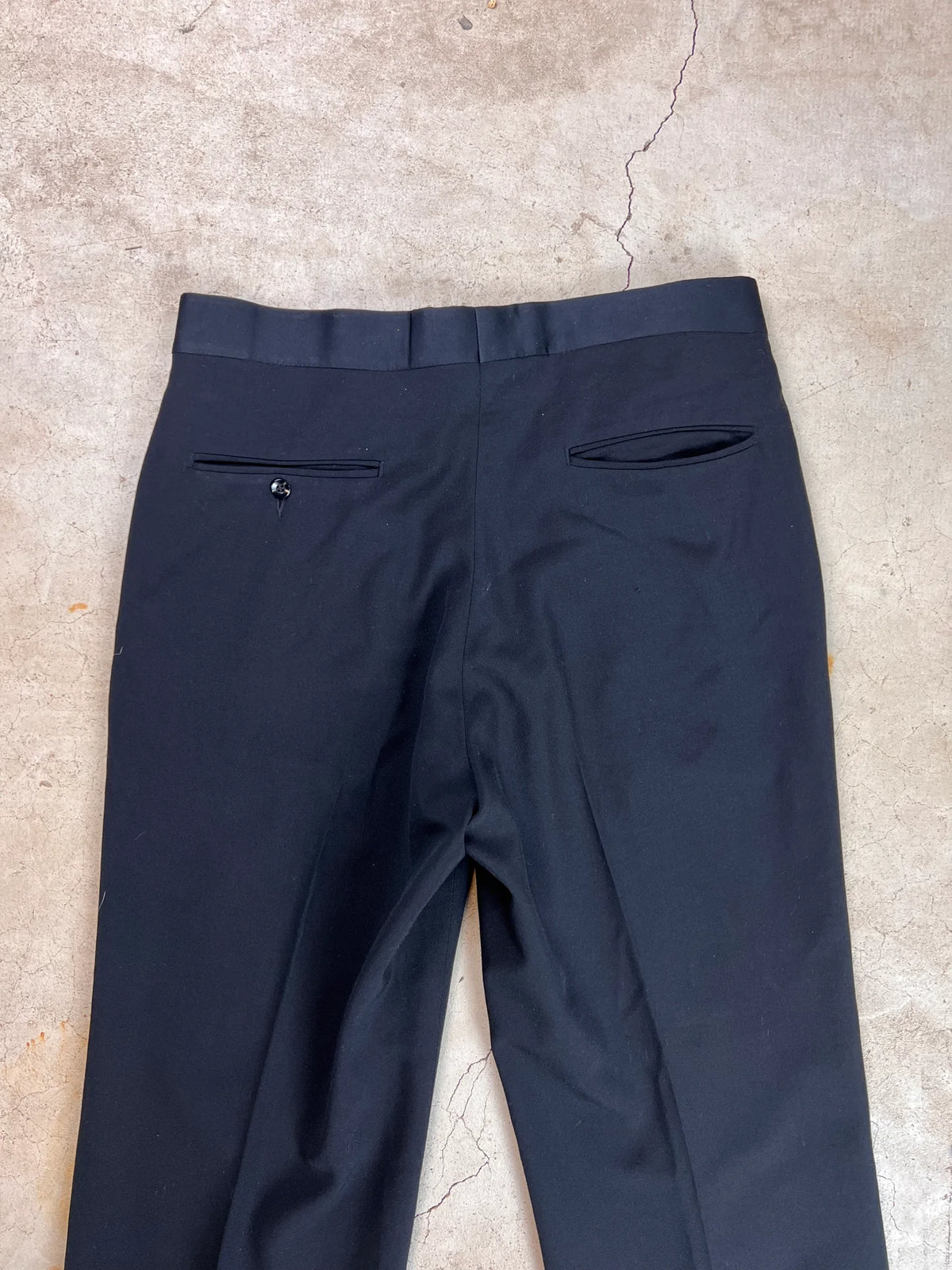Black trousers laid out on a textured surface.