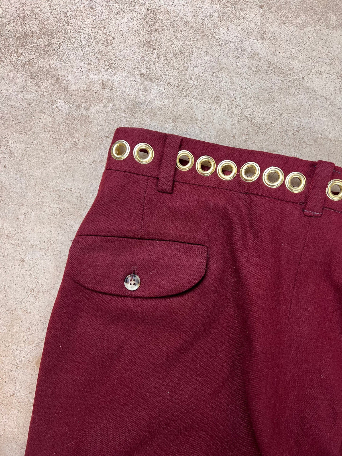 Burgundy trousers with grommet belt loops and a buttoned back pocket.