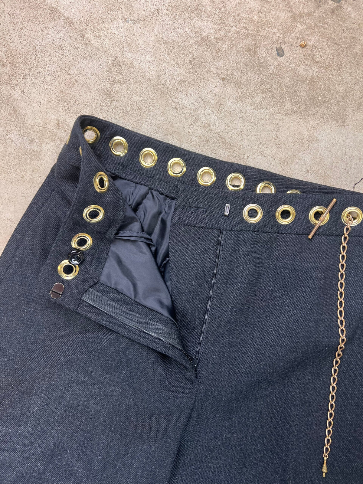 Navy blue trousers with a high waist embellished with gold-tone grommets and a decorative chain.