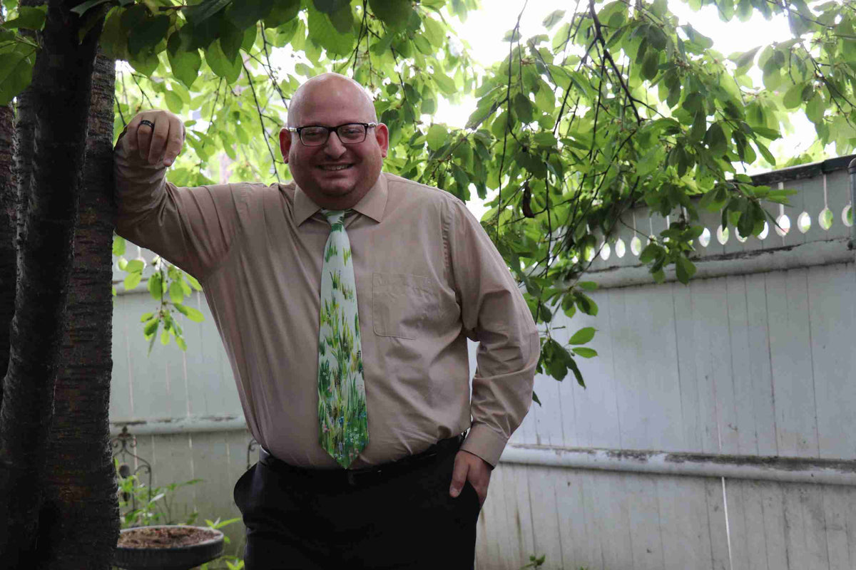 a man wearing a tie standing next to a tree.