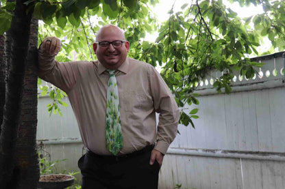 a man wearing a tie standing next to a tree.