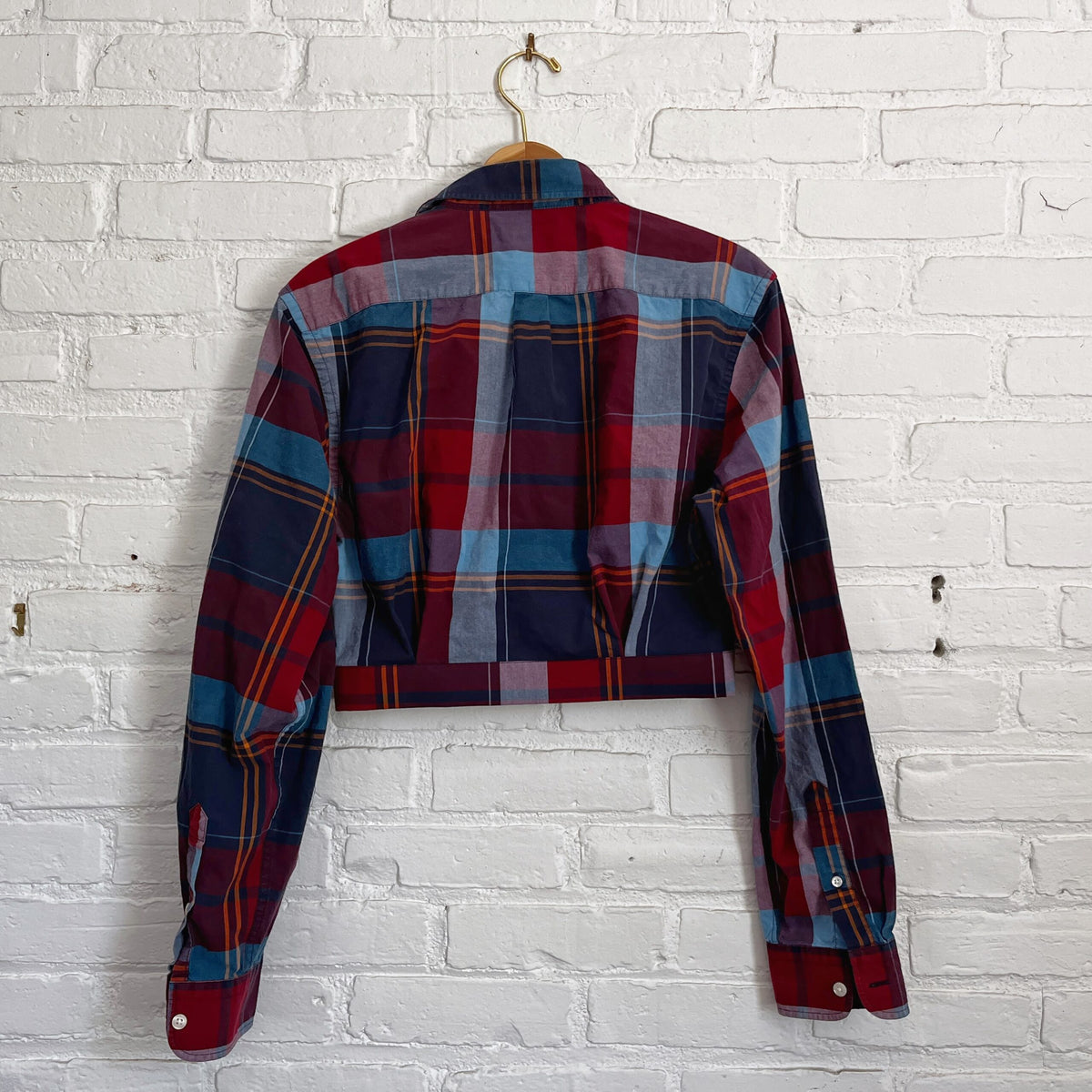 A red and blue plaid shirt hanging on a brick wall.