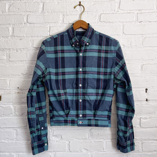 A blue and green plaid shirt hanging on a brick wall.