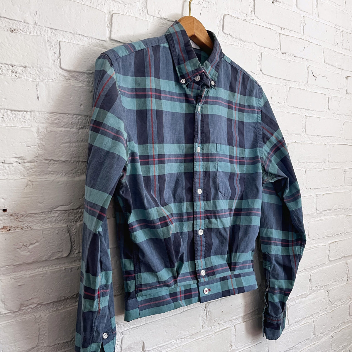 A blue and green plaid shirt hanging on a brick wall.