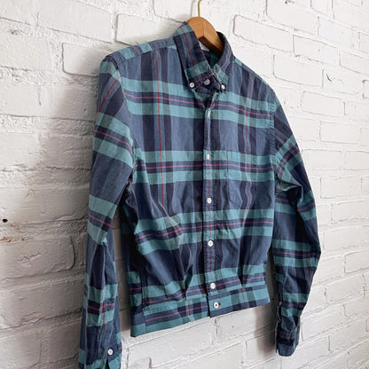 A blue and green plaid shirt hanging on a brick wall.