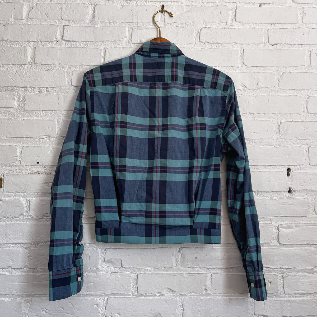 A blue and green plaid shirt hanging on a brick wall.