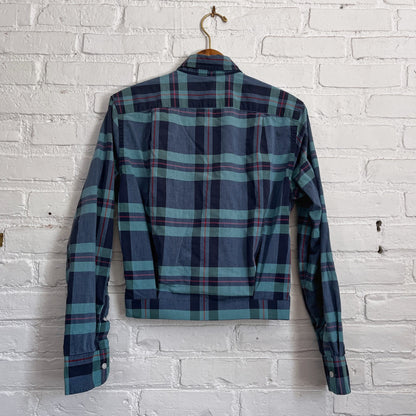 A blue and green plaid shirt hanging on a brick wall.