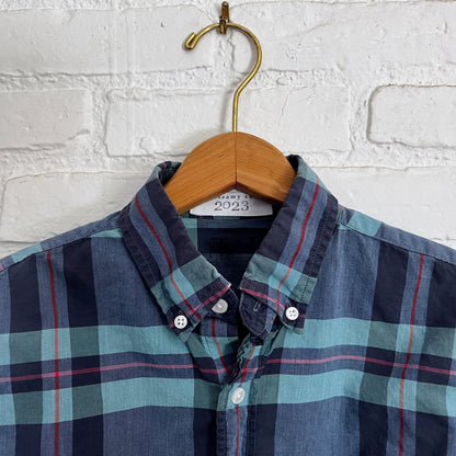 A blue and red plaid shirt hanging on a white brick wall.
