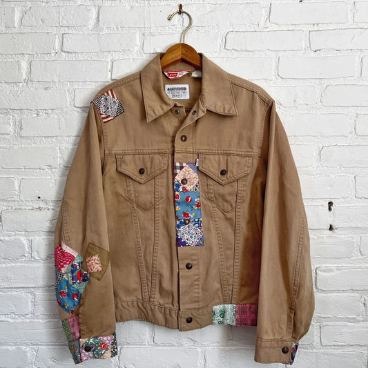 A tan jacket with colorful patches hanging on a brick wall.