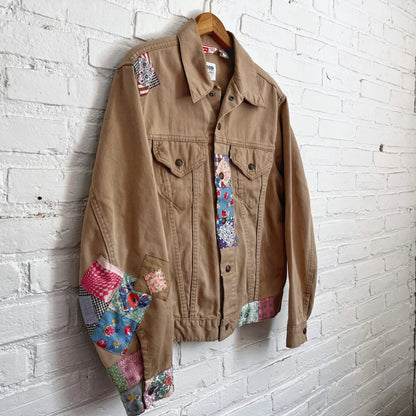 A patchwork denim jacket hanging on a brick wall.