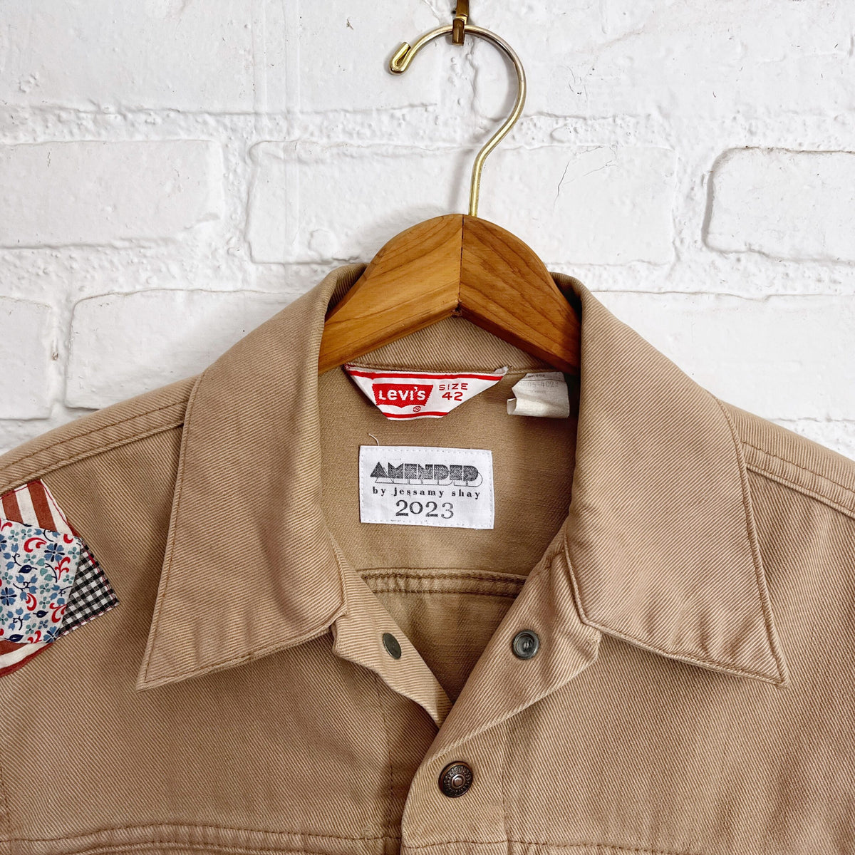 A tan jacket hanging on a brick wall.