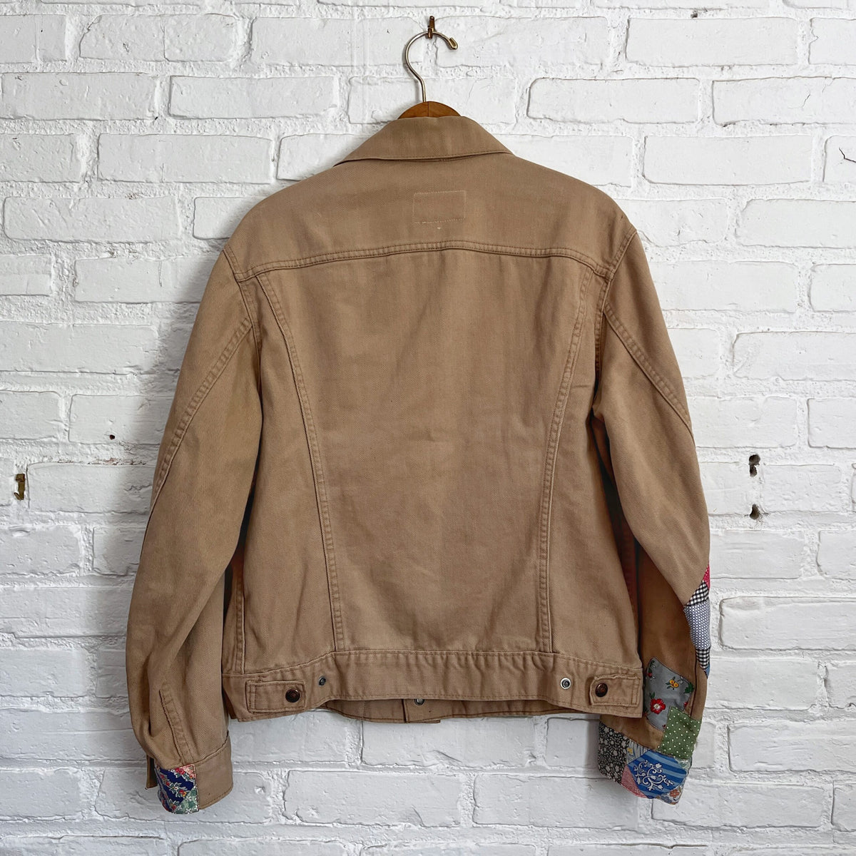 A tan jacket hanging on a brick wall.