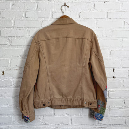 A tan jacket hanging on a brick wall.