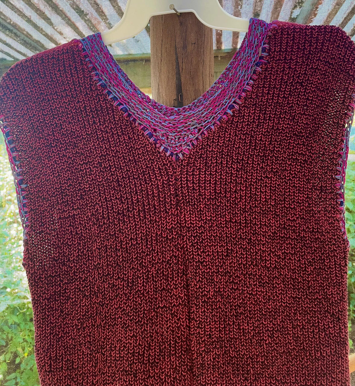 A burgundy knitted vest hanging on a wooden hanger.