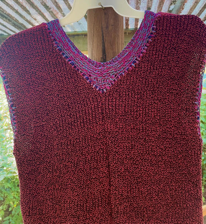 A burgundy knitted vest hanging on a wooden hanger.