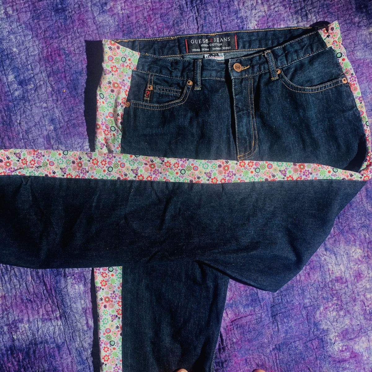 a pair of jeans sitting on top of a purple blanket.