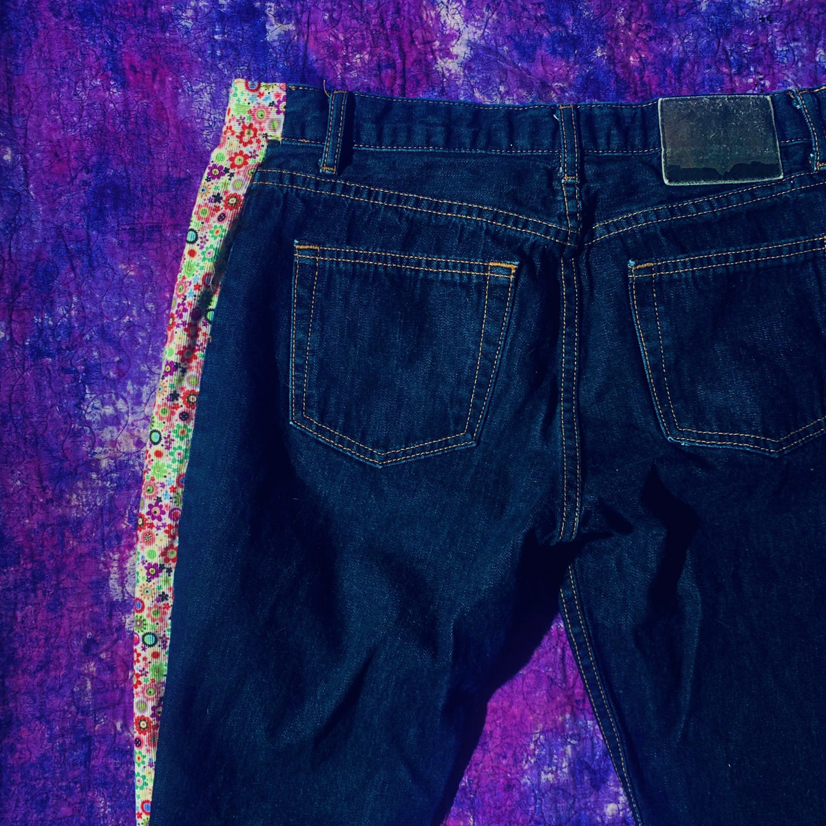 a pair of jeans sitting on top of a purple blanket.