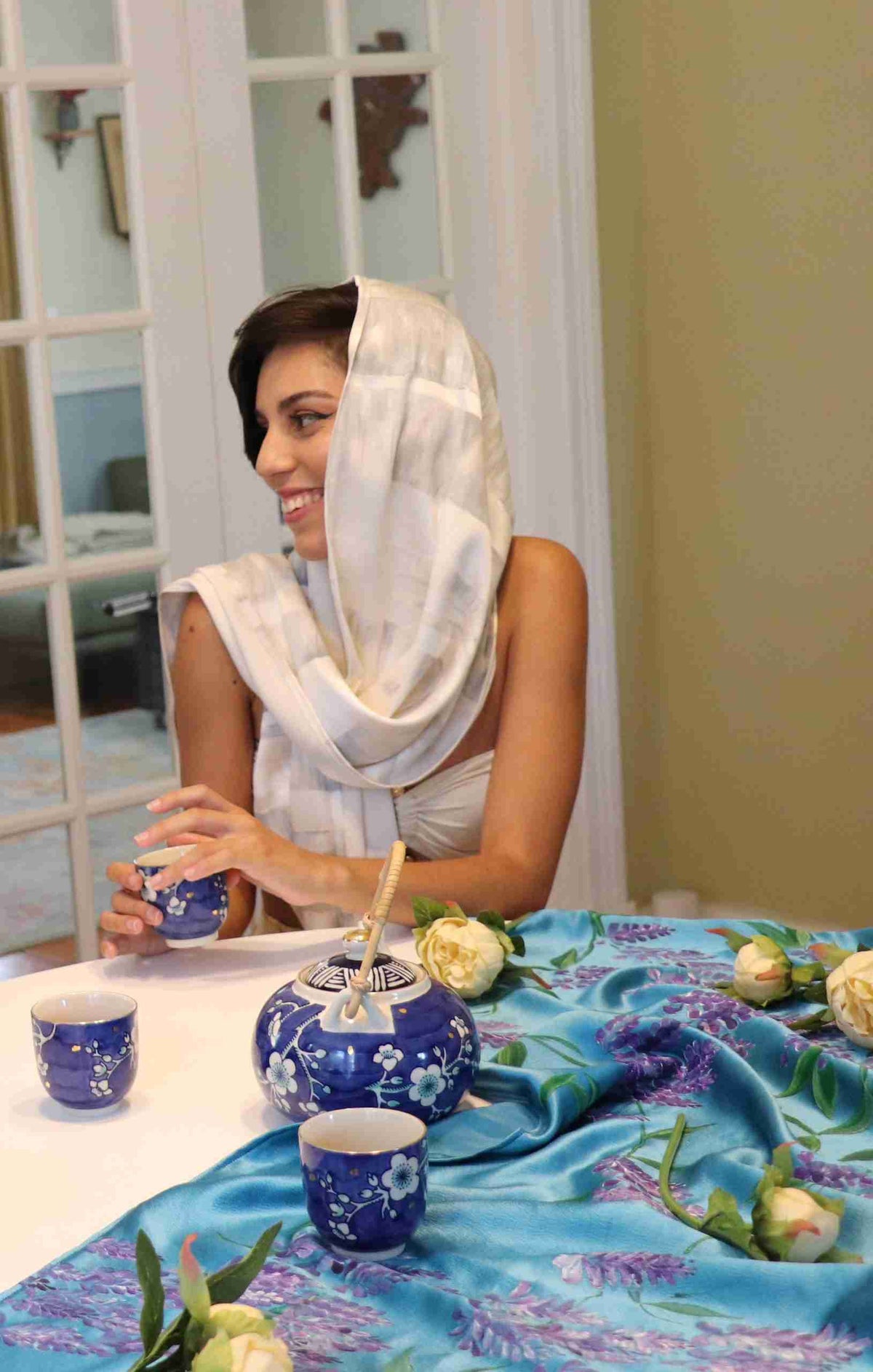 a woman sitting at a table with a blue vase.