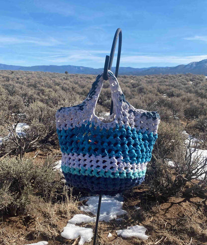 a blue and white crocheted bag sitting on top of a snow covered ground.