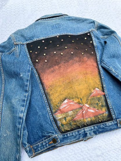 A denim jacket with a painting on the back.