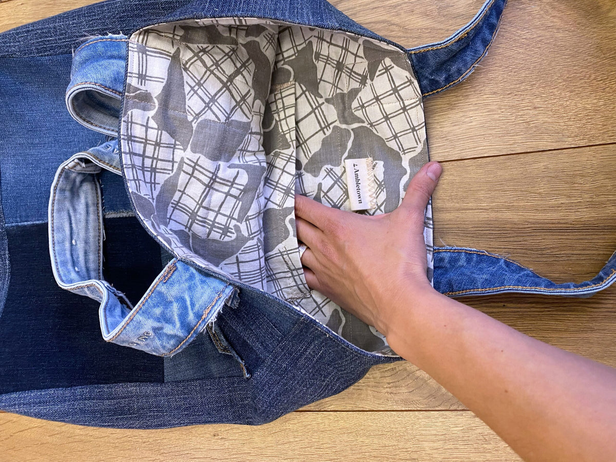 A person opening a denim tote bag on a wooden floor.